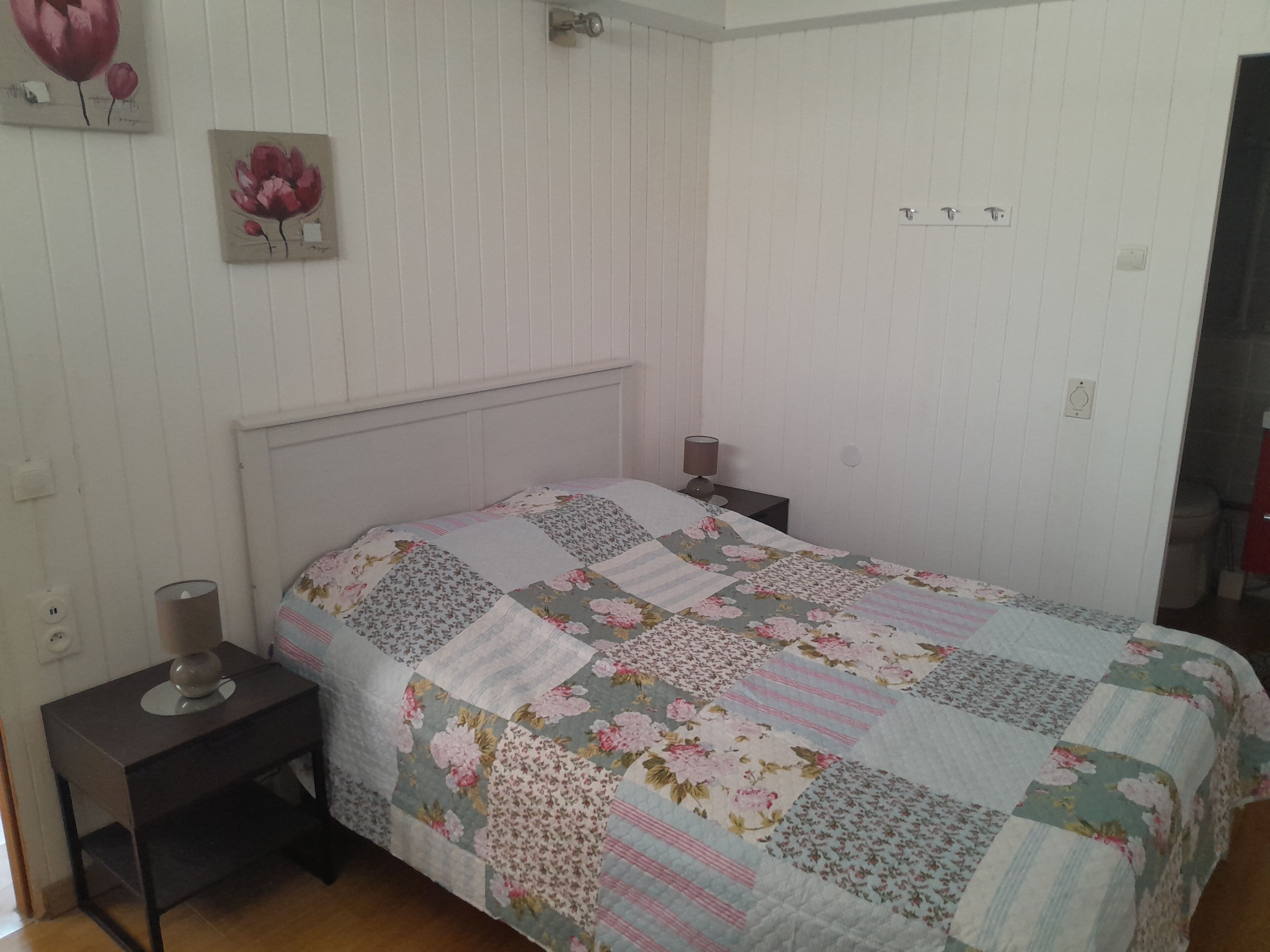 Une chambre à coucher avec un lit, des tables de chevet, une lampe et un mur orné d’un tableau représentant des motifs floraux.