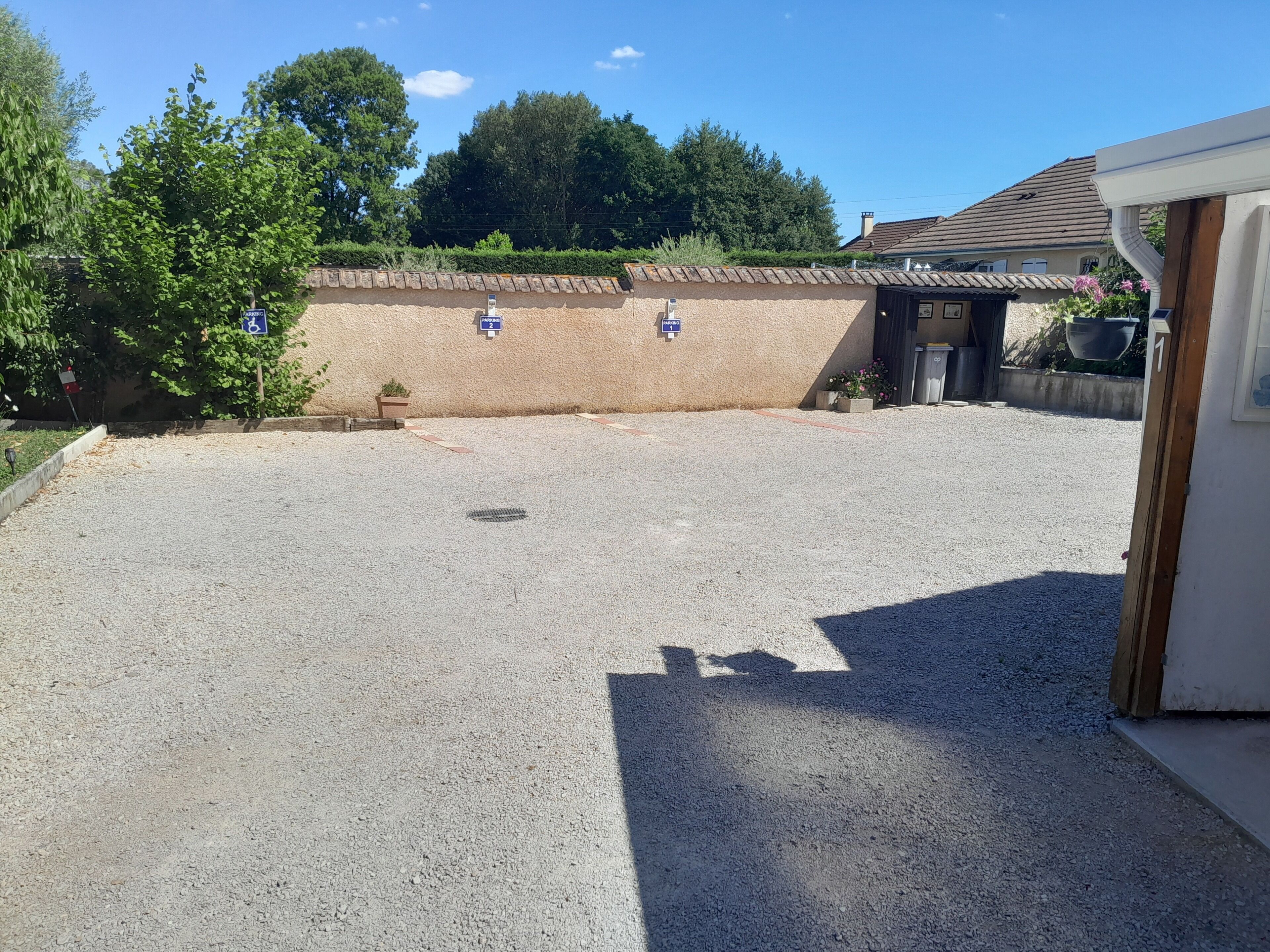 A gravel parking area with a building entrance, a wall with a door, and a tree.