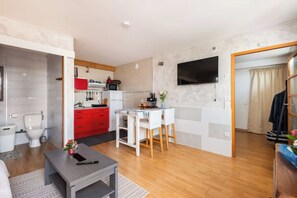 A compact living space with a kitchenette, a dining area, a TV mounted on the wall, and a visible door leading to another room.
