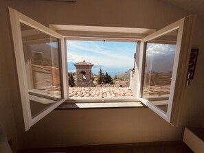A room with an open window revealing a view of a stone tower and a mountainous landscape. - La finestra sul Lago by Theater Home - with marvellous lake view (Tignale)