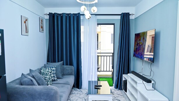 Ein modernes Wohnzimmer mit grauem Sofa, einem Couchtisch, einem Flachbildfernseher und Blick auf einen Balkon.