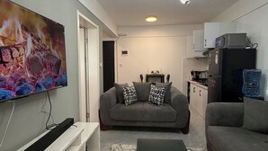 Ein Wohnzimmer mit Flachbildfernseher, einer Couch, einem Couchtisch und einer Küche im Hintergrund.