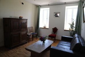 A living room with a wooden cabinet, a sofa, a coffee table with a vase, a chair, and a window with curtains. - Vrbo Property (Morbach)