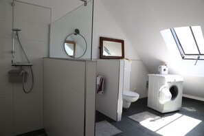 A modern bathroom with a shower, toilet, and washing machine, featuring a skylight and tiled walls. - Vrbo Property (Morbach)