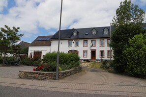 A two-story building with a stone foundation, a red door, and a small garden area with red flowers. - Vrbo Property (Morbach)