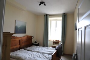 A bedroom with two beds, a nightstand, a chair, a window with curtains, and a ceiling fan. - Vrbo Property (Morbach)