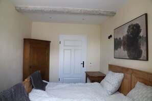 A bedroom with a bed, a wooden wardrobe, a white door, a small table, and a painting on the wall.