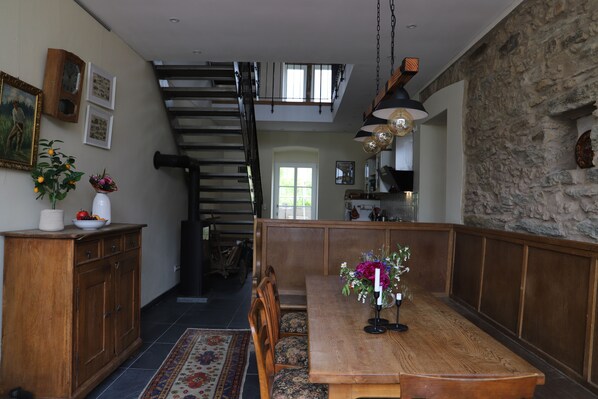 A dining area with a wooden table, chairs, and a bench. There is a staircase leading to an upper level, a stone wall, and a hanging light fixture. - Vrbo Property (Morbach)