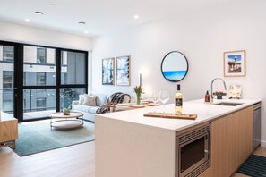Eine moderne Küche mit Kochinsel, ein Essbereich mit rundem Tisch und ein Wohnzimmer mit einer Couch.