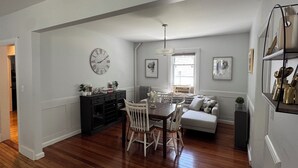 A dining area with a wooden table and chairs, a black console, and a white sofa.