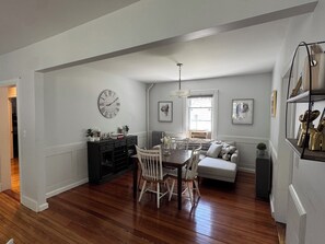 A dining area with a wooden table and chairs, a black console, and a white sofa. - FIFA World Cup Stay. Near I-95 & Route 1 (North Attleborough)