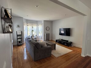 Uma sala de estar moderna com um sofá modular cinza, uma TV de tela plana e piso de madeira.
