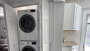 A laundry room with two stacked front-loading washing machines, a white door, and a kitchen area with a countertop and cabinets.