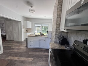 A modern kitchen with white cabinets, a granite countertop, a stainless steel range, and a large window. - FIFA World Cup Stay. Near I-95 & Route 1 (North Attleborough)