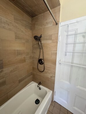 Ein Badezimmer mit Dusche, Badewanne und einer weißen Tür.