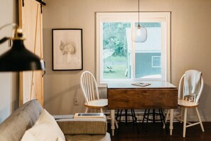 A dining area with a wooden table, white chairs, a hanging light fixture, and a framed picture on the wall.