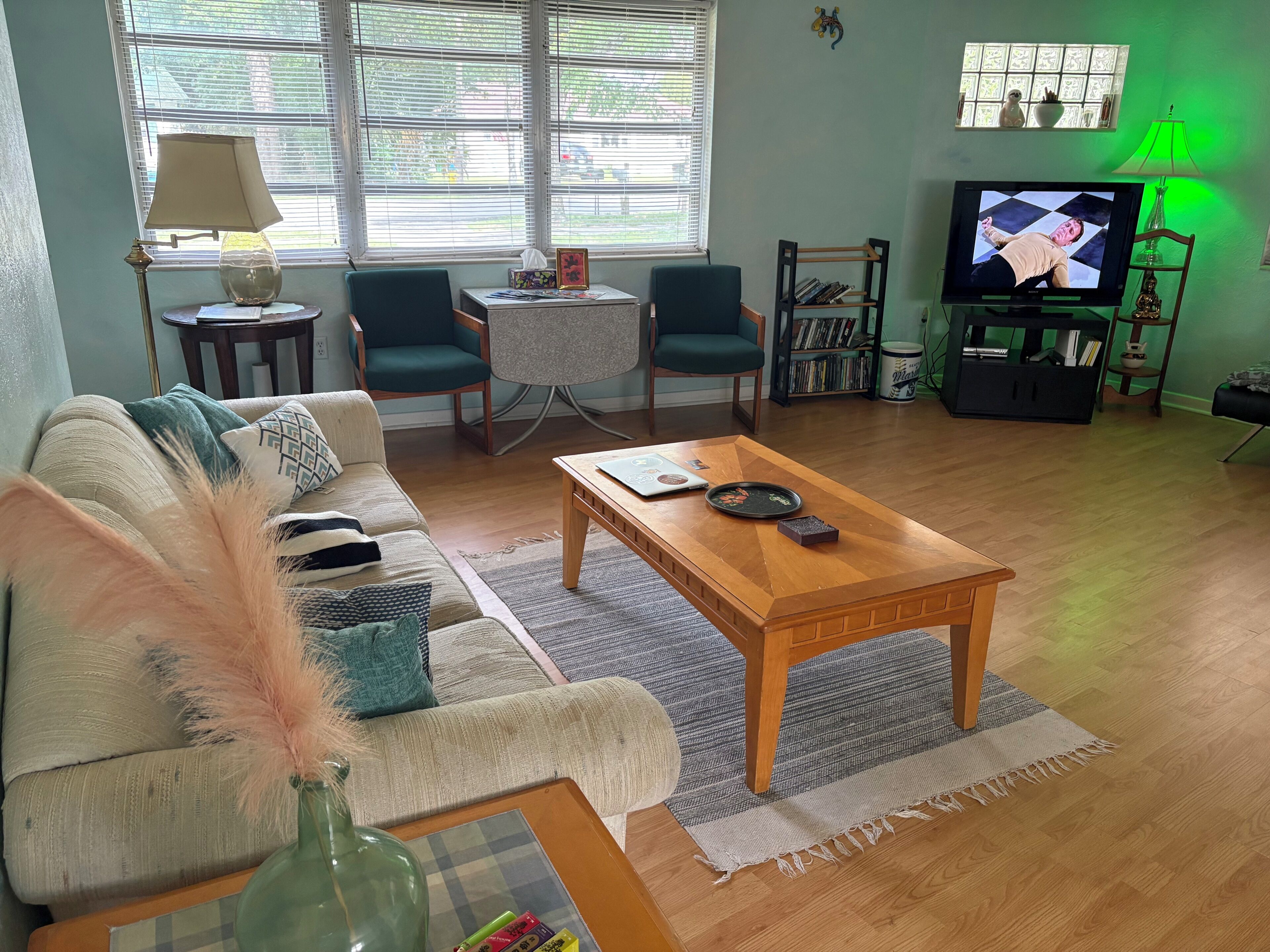 A living room with a sofa, two chairs, a coffee table, a TV, a lamp, and a bookshelf.