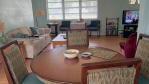 Een woonkamer met een ronde tafel, twee stoelen, een bank, een televisie en een boekenkast.