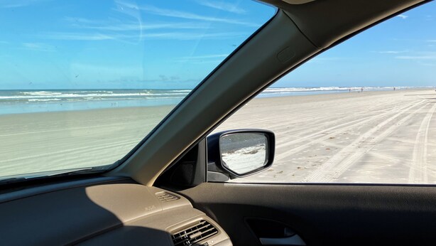 Autobinnenkant met uitzicht op een strand door het raam.