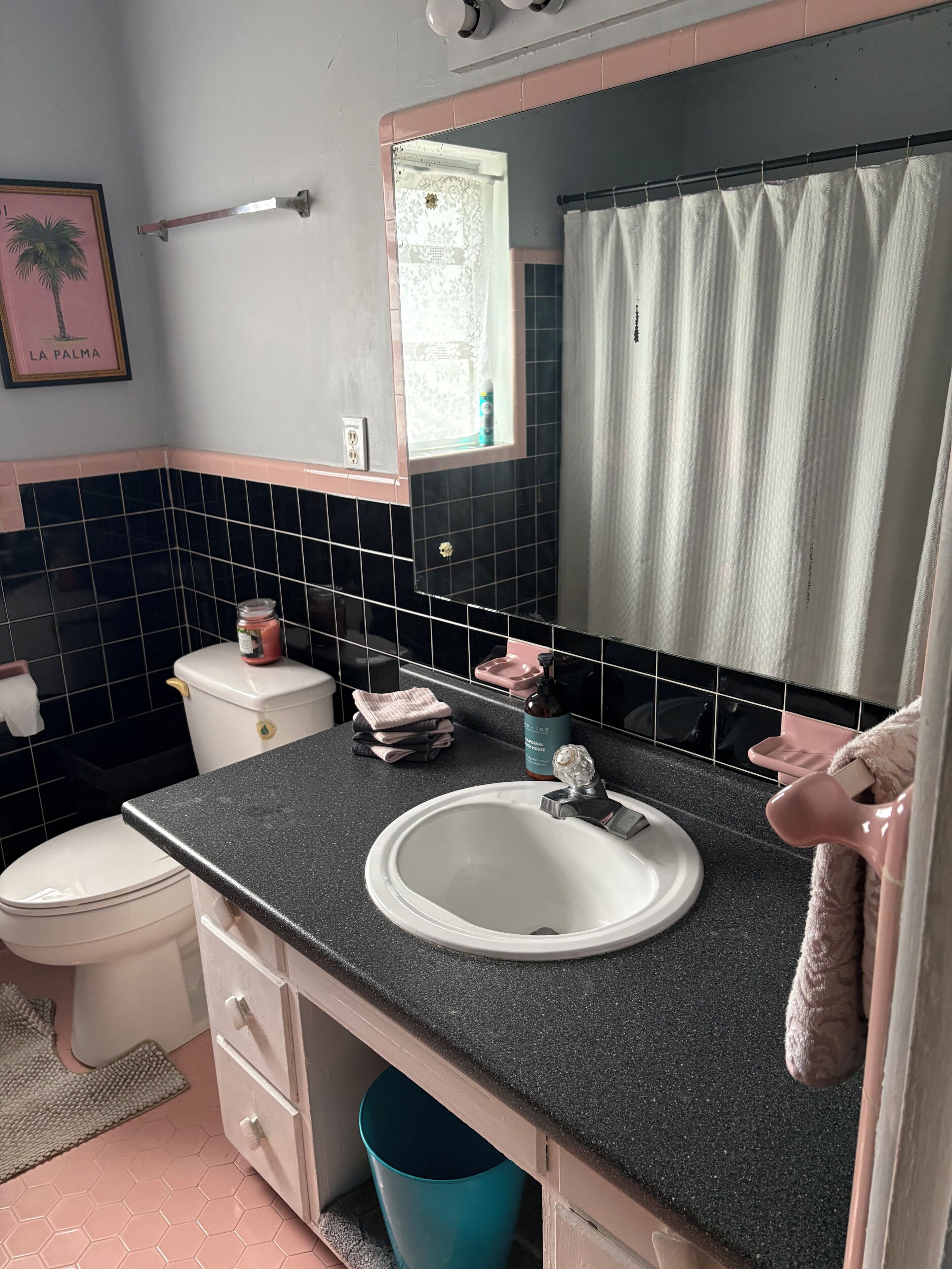Een badkamer met een witte wastafel, een spiegel, een toilet en een blauwe prullenbak.
