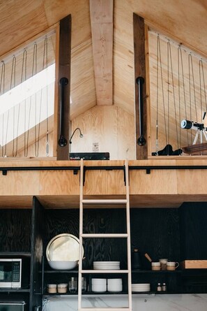 Ein Loft-Zimmer mit Holzbalkendecke, einem Teleskop und einer Leitern.