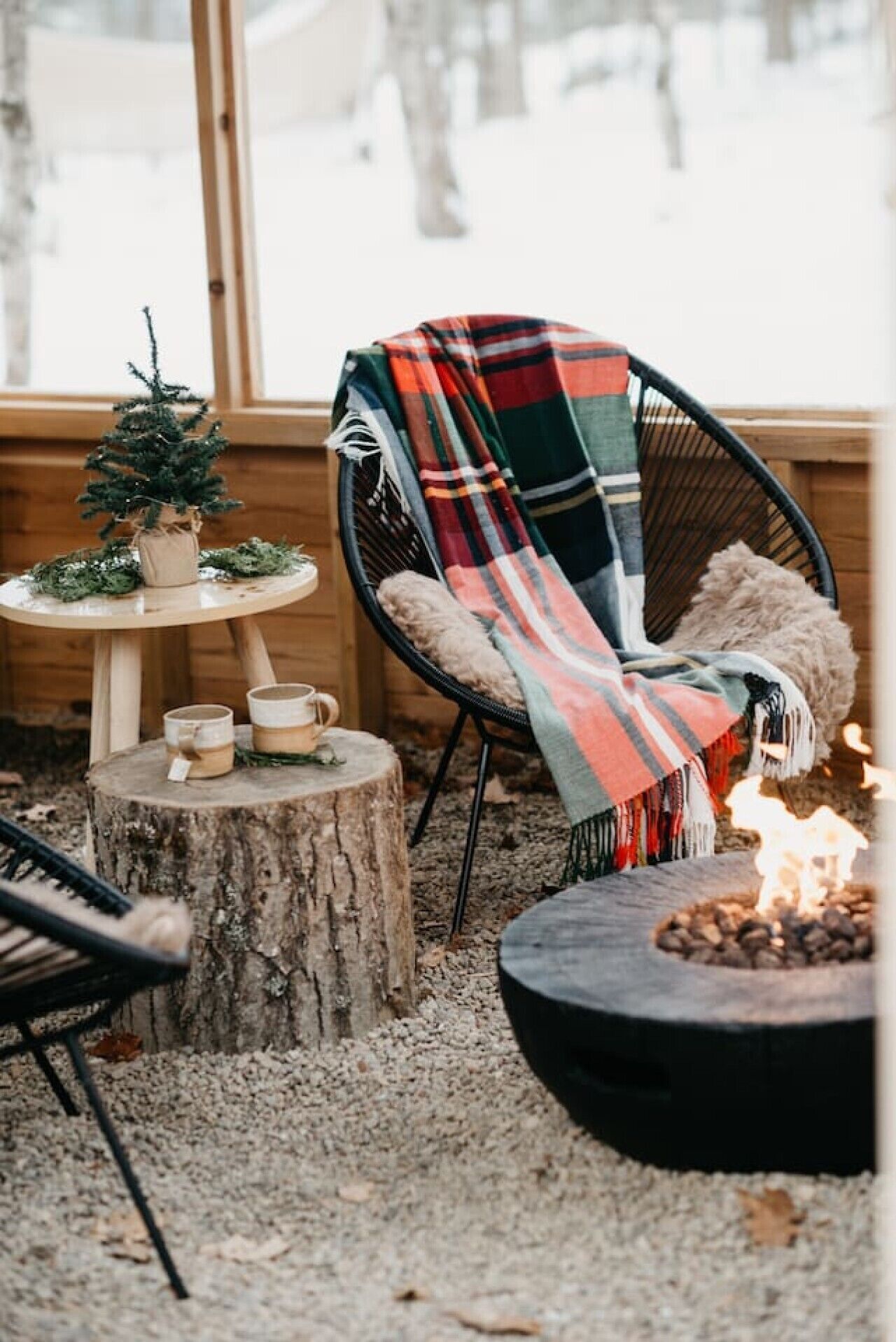 Un espace extérieur accueillant, aménagé avec une chaise, une petite table, un tronc d’arbre et un foyer.