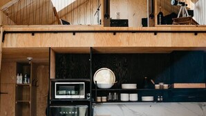 Une cuisine compacte dotée d’un four, d’un micro-ondes et d’un évier intégrés, de meubles de rangement en bois et d’un petit coin repas.
