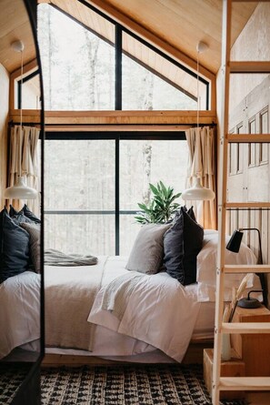 Ein gemütliches Schlafzimmer mit großem Fenster, einem Bett, einem Nachttisch und einer Pflanze.