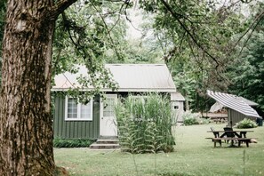 Eine rustikale Holzhütte mit grüner Fassade, einer Veranda und einem Picknicktisch im Garten.