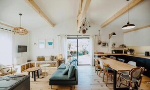 Un salón amplio con sofá, mesa de comedor y sillas, vigas de madera y un ventanal grande.