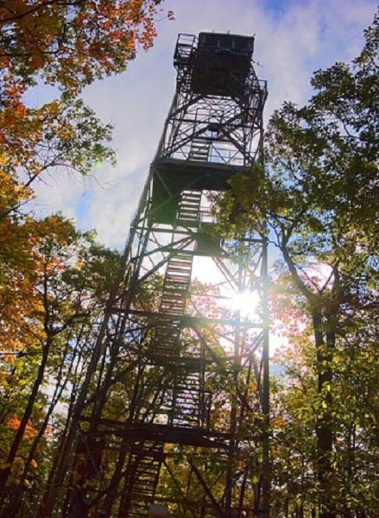 A tall metal structure with a staircase, surrounded by trees with autumn foliage.