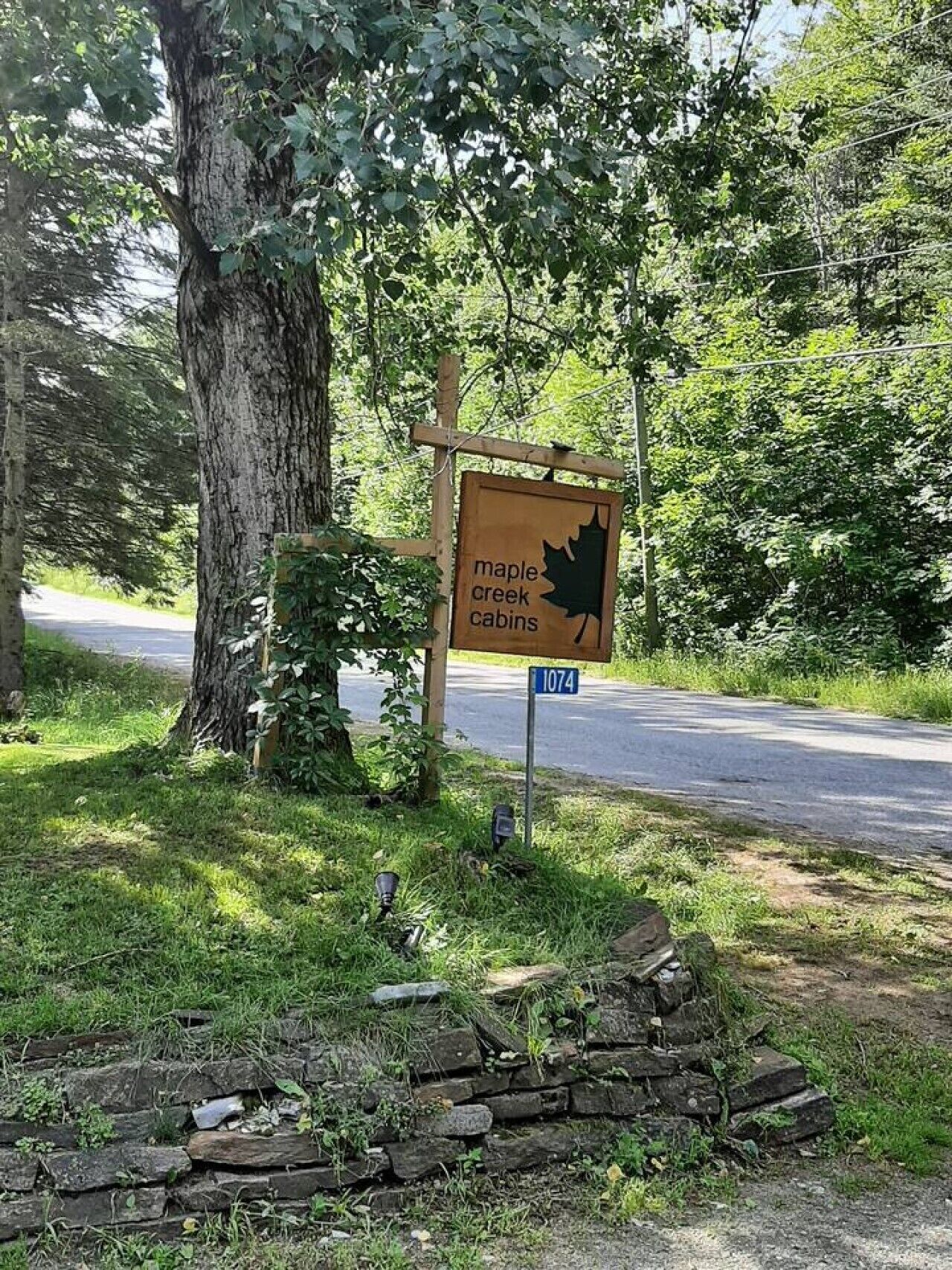 Schild für die Maple Creek Cabins mit einem Ahornblatt-Logo, einer Steinmauer und einer Straße im Hintergrund.