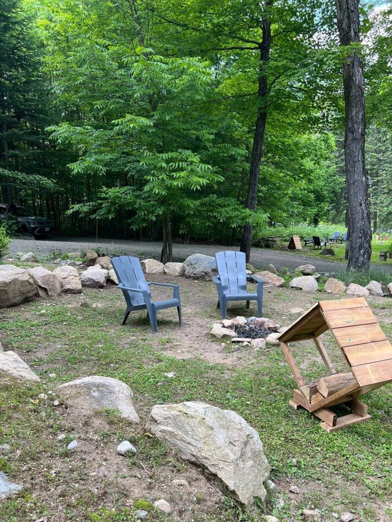 Een camping met twee blauwe stoelen, een houten vuurplaats en een bebost achtergrond.