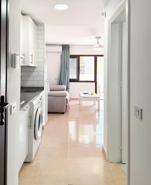 Une cuisine compacte équipée d’un lave-linge, d’un canapé et d’une petite table.