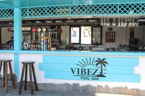 A pool bar with a sign reading 'VIBEZ POOL BAR,' bar stools, a counter with various bottles, and a window. - Amazing Oasis Dunas Wi-Fi and Air Conditioning by B-Rent (Corralejo)