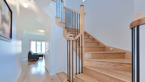 Un interior moderno con una escalera de madera, una zona de estar con sofá y un cuadro en la pared.