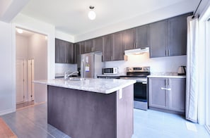 A modern kitchen with dark cabinets, stainless steel appliances, and a marble countertop.