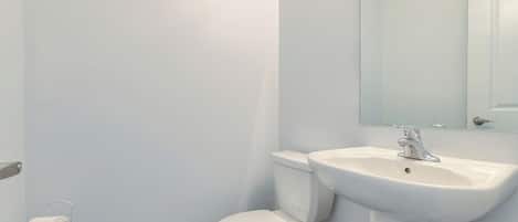 A bathroom with a toilet, sink, and mirror.