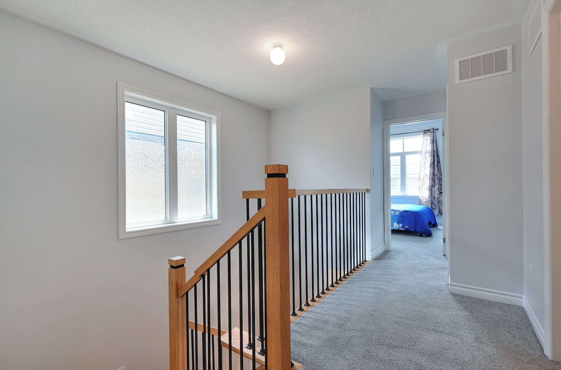 A hallway with a wooden staircase, a carpeted floor, and a window with blinds.