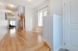 A spacious hallway with wooden flooring, a staircase, and a door.