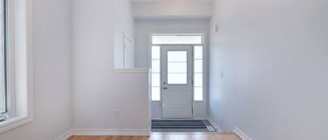A hallway with wooden flooring, a white door, and a window on the left.