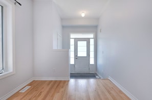 A hallway with wooden flooring, a white door, and a window on the left.