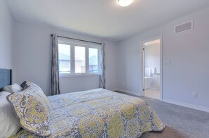 Ein Schlafzimmer mit Bett, Fenster, einer Tür zum Badezimmer und einem Deckenventil.