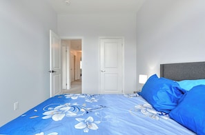 A bedroom with a bed, pillows, a nightstand, and a door leading to another room.