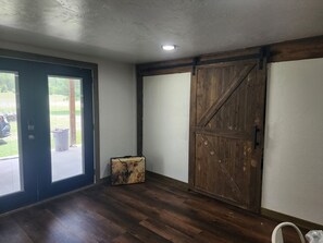 Ein Zimmer mit einer dunklen Holztür, einer großen, stallartigen Holztür und einem Koffer auf dem Boden.