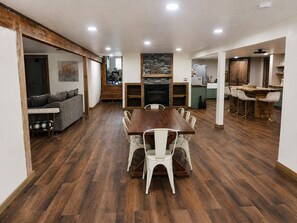 Ein geräumiger Essbereich mit einem langen Holztisch und weißen Stühlen, eine Küche mit Steinrückwand und eine gemütliche Sitzecke mit einer Couch und Kissen.