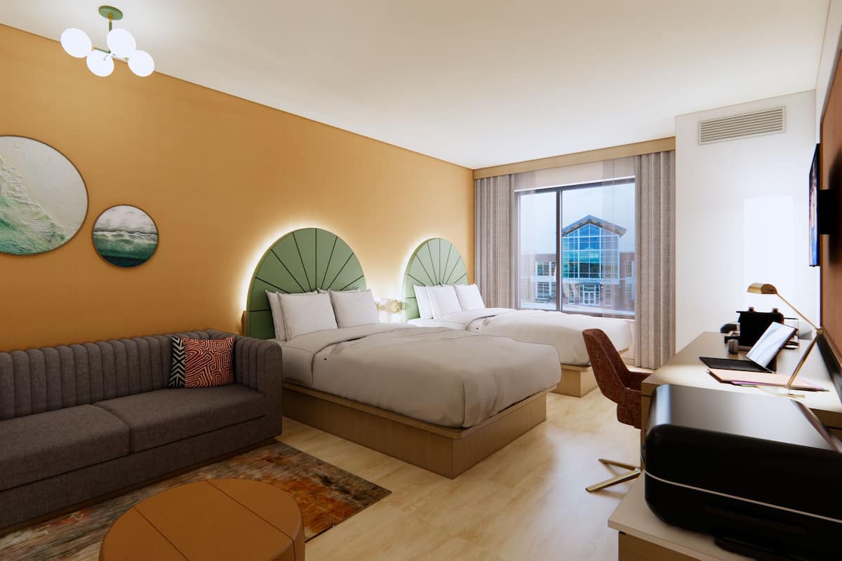 A hotel room with a sofa, two beds, a desk with a laptop, and artwork on the wall.