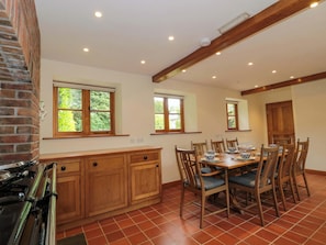 A kitchen with a stove, wooden cabinets, and a dining area with a table and chairs. - Stowey Mead Stables (Bristol)