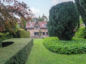 A stone house with a tiled roof, surrounded by well-maintained hedges and a neatly trimmed lawn. - Stowey Mead Stables (Bristol)