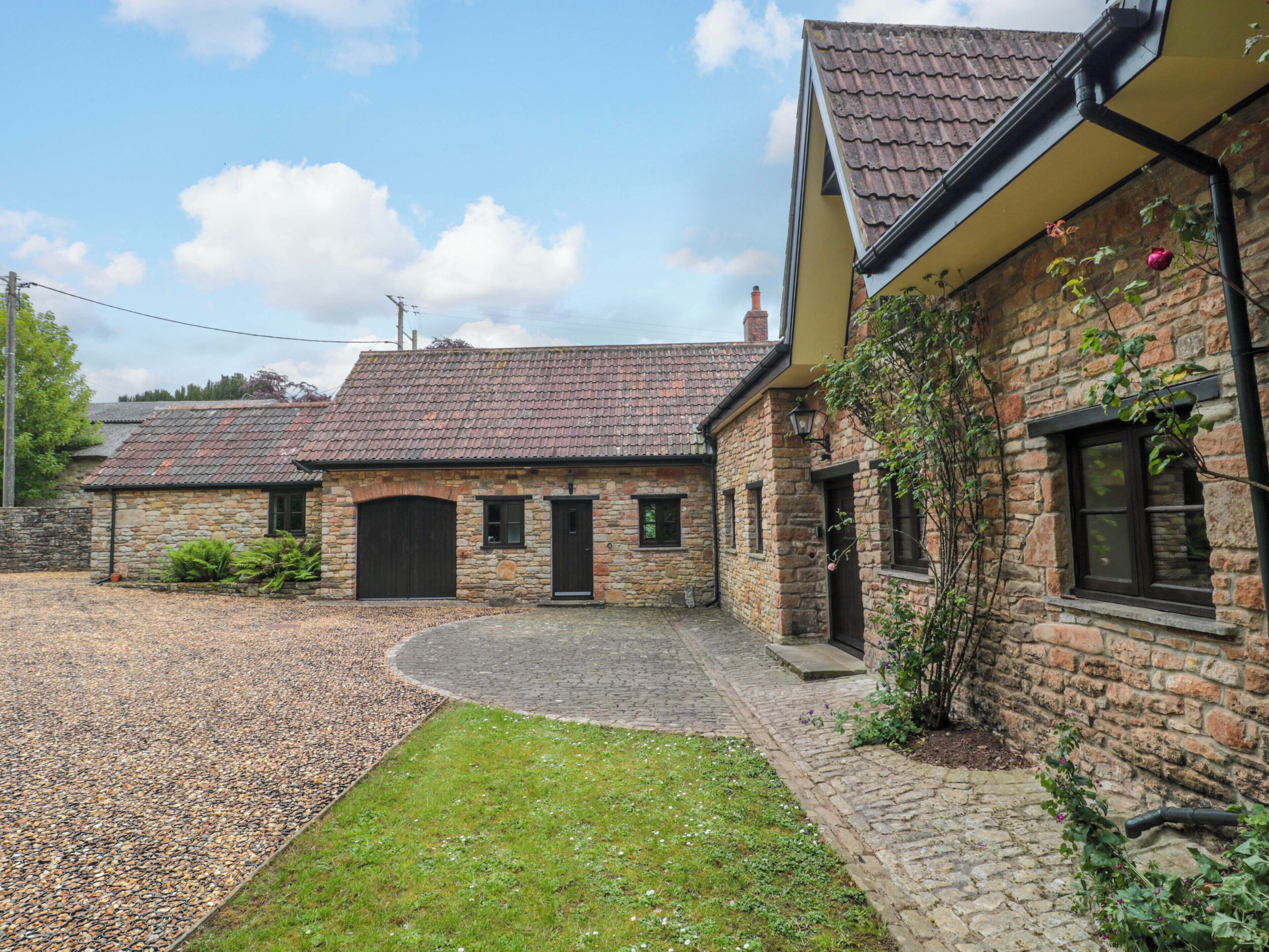A stone house with a tiled roof, a gravel driveway, and a grassy lawn.